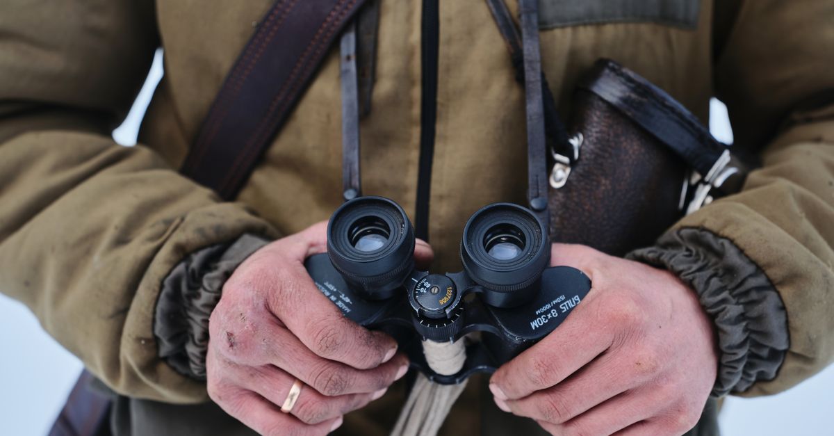 A person in a jacket holds binoculars outdoors, emphasizing adventure and exploration.